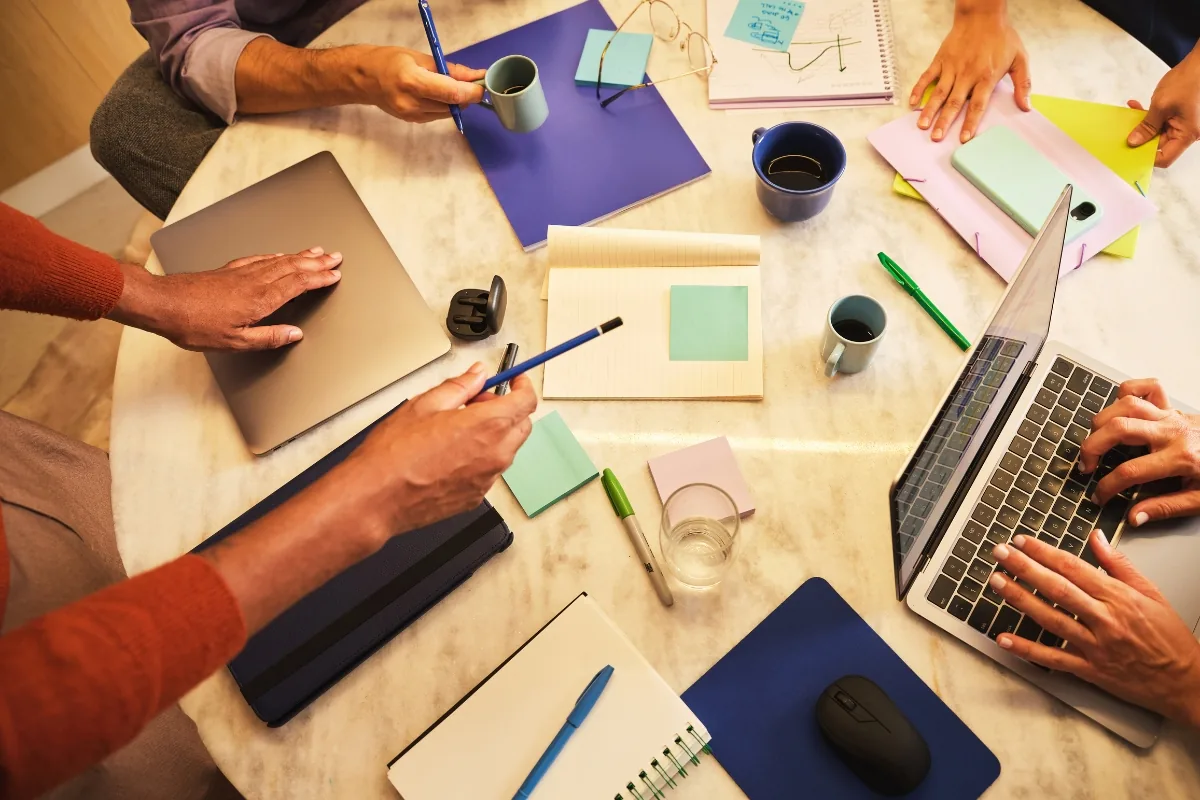 A team working together around a table with laptops, notebooks and shared notes